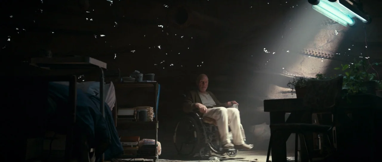 Logan (2017) movie still: wide — A dark, cramped bunker interior features peeling walls and scattered household items in the gloom. An elderly man…