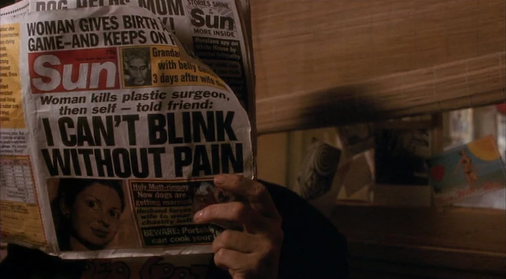 The Fisher King (1991) movie still: closeup — A person holds a tabloid newspaper featuring sensationalist headlines directly in front of their face.…