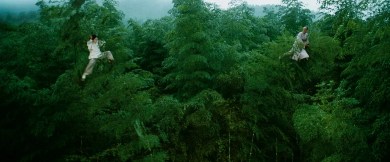 Crouching Tiger, Hidden Dragon (2000) movie still: wide — A dense green bamboo forest stretches across the frame under an overcast sky. Two men in…