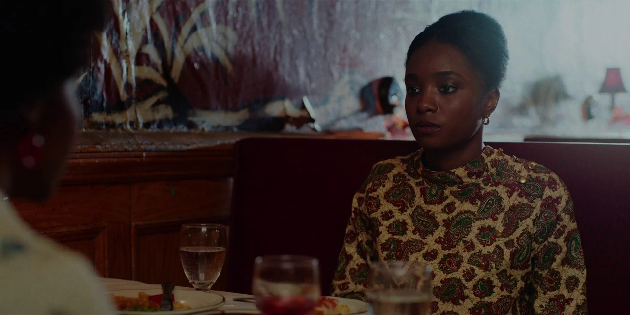 If Beale Street Could Talk (2018) movie still: medium — A dimly lit diner booth features red vinyl seating and patterned wallpaper. A young Black…