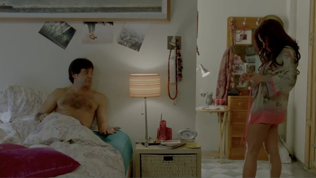 George Lopez: It's Not Me, It's You (2012) movie still: medium — A cluttered apartment bedroom with a bed, a bedside table, and various wall…