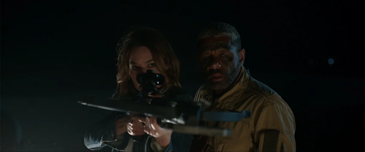 An Endless Wedding (2025) movie still: medium — A dark outdoor space at night with no visible background details. A woman aims a crossbow while a…