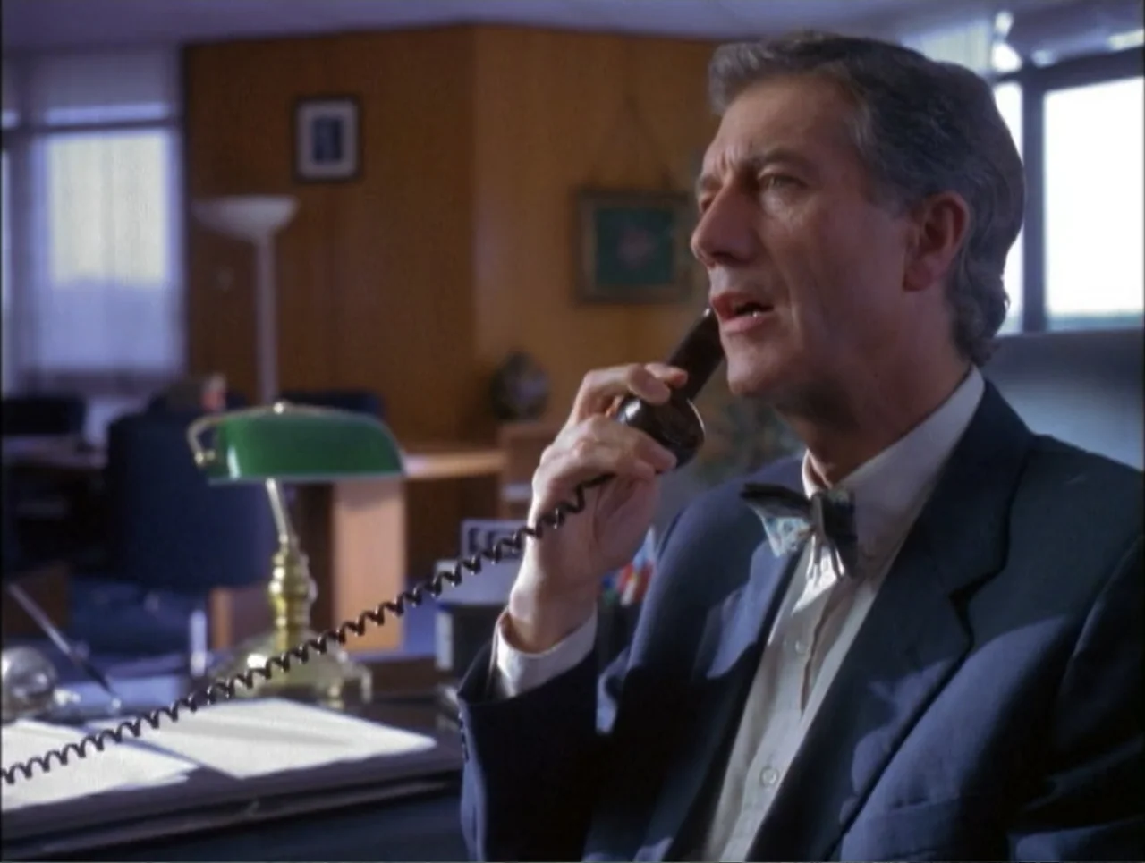 Code Name: Wolverine (1996) movie still: medium — An office with wood paneled walls features a dark desk and a green banker lamp. An older man in a…