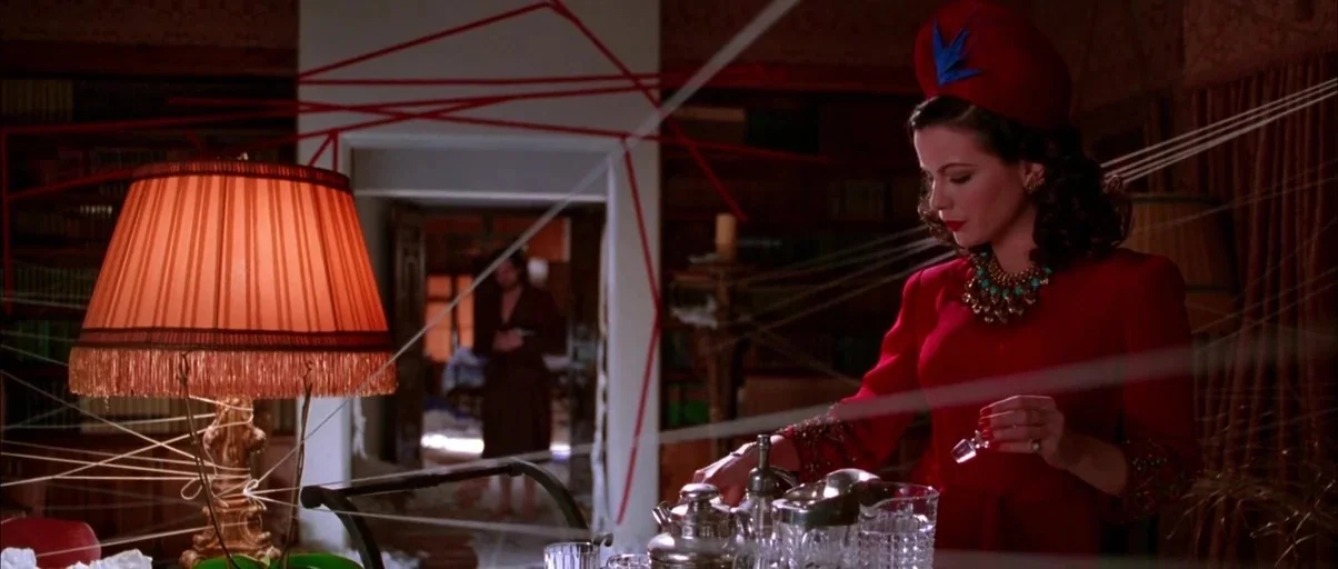 The Aviator (2004) movie still: medium — A dimly lit room filled with complex webs of red and white string. A woman in a red hat stands in the…