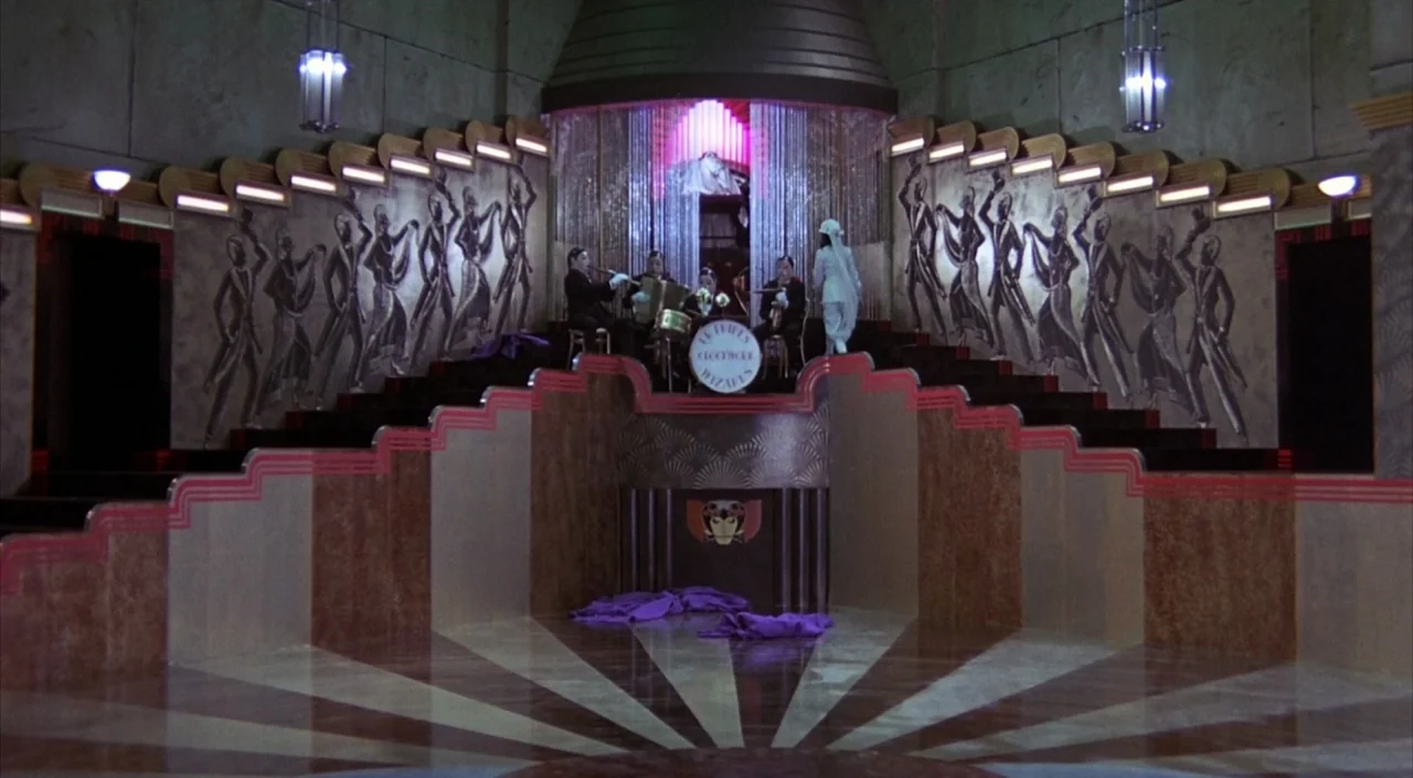 Dr. Phibes Rises Again (1972) movie still: wide — An Art Deco ballroom features tiered stairs, metallic wall panels, and patterned floor tiling. A…