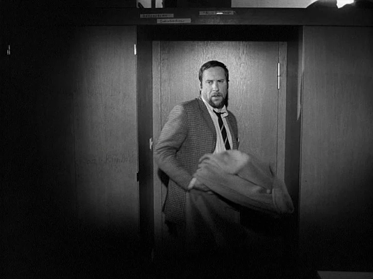 Gods Of The Plague (1970) movie still: medium — A man stands in a dark doorway flanked by plain wooden paneling. The subject emerges from the frame…