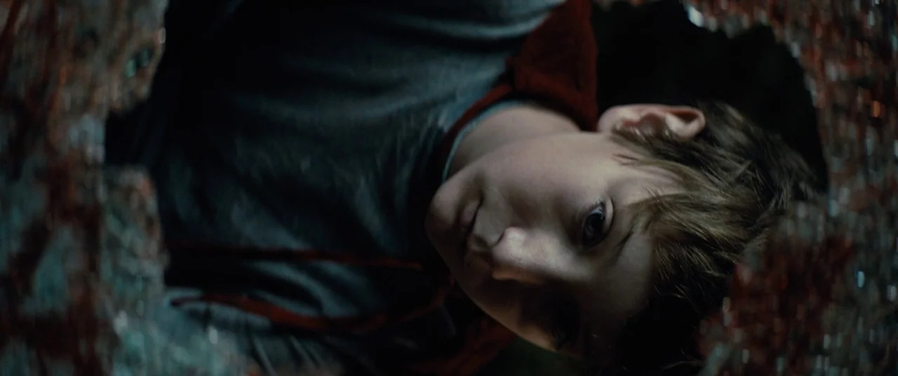 Brightburn (2019) movie still: closeup — A child lies inside a dark, confined space with jagged, fractured reflective surfaces visible. The child's…