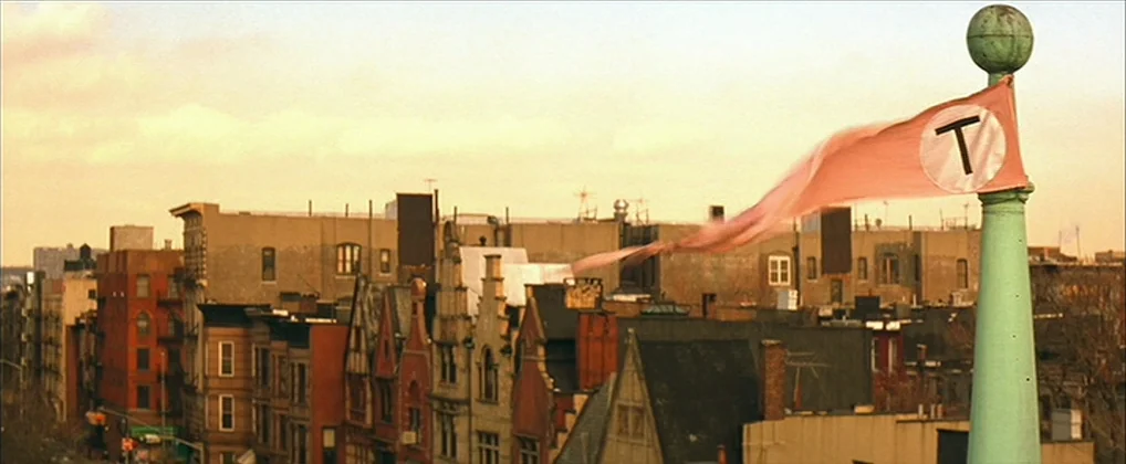 The Royal Tenenbaums (2001) movie still: establishing — An urban cityscape with rows of apartment buildings under a hazy, warm sky. A mint green…