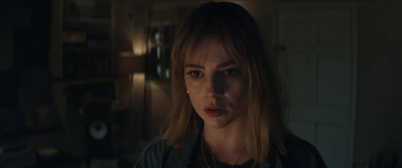 The Greatest Hits (2024) movie still: closeup — A dimly lit room at night features soft background lamps and dark shadows. A young woman with…