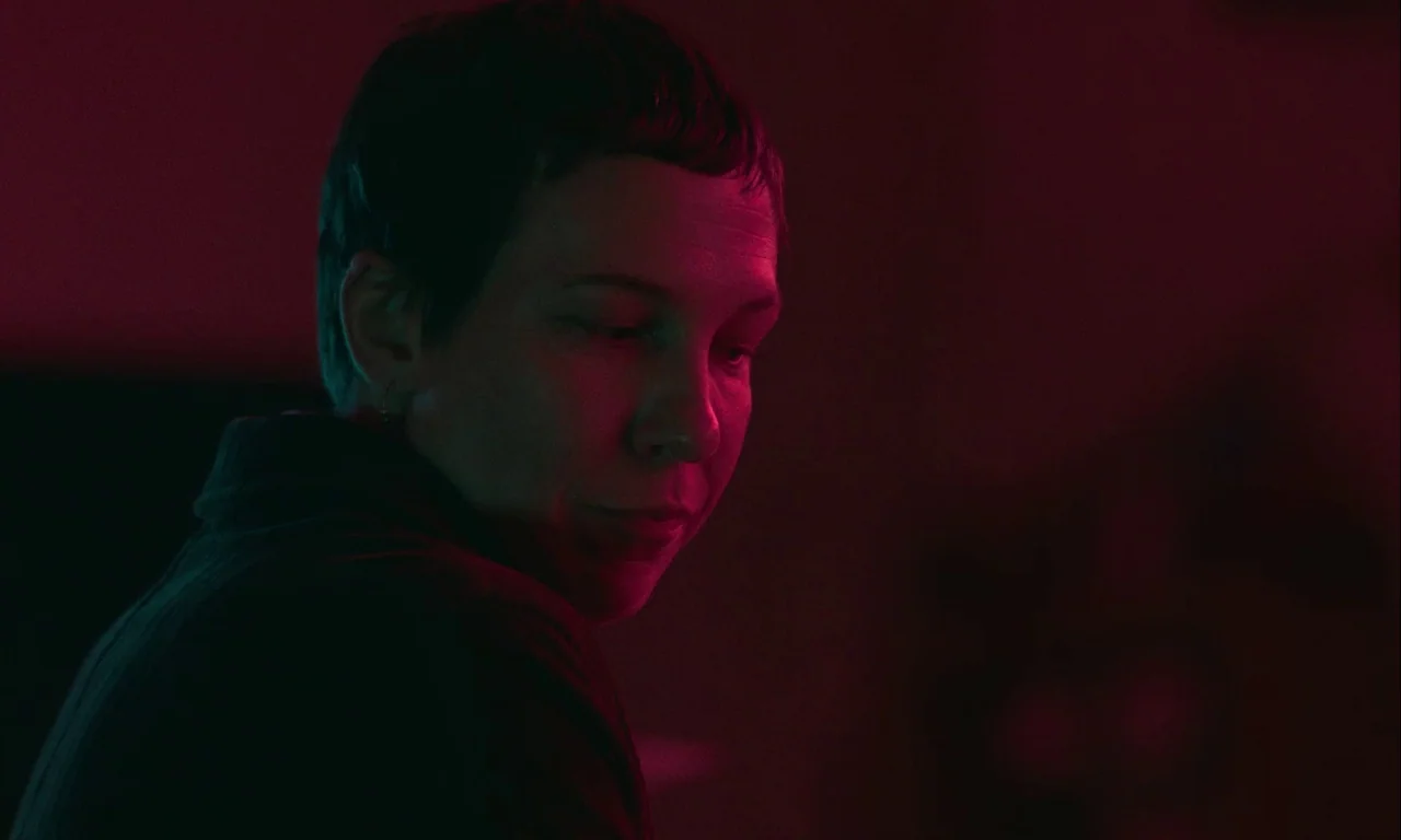 Mickey and the Bear (2019) movie still: closeup — A dark, dimly lit interior space is suffused with a deep red light. A woman with short dark hair…