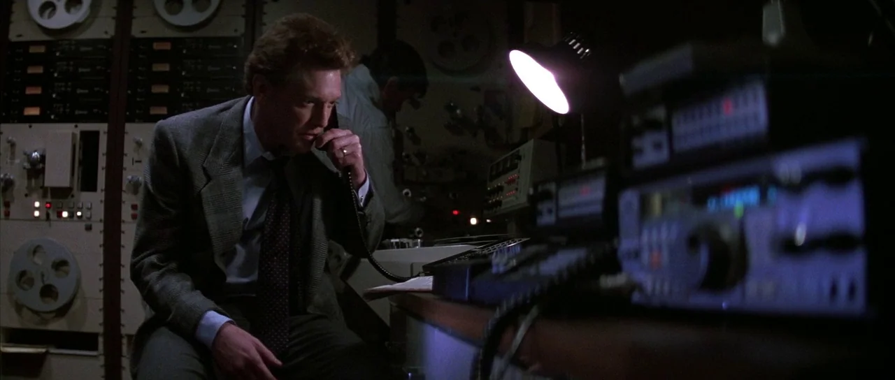 Die Hard (1988) movie still: medium — A dark room is filled with large 1980s reel-to-reel magnetic tape recording equipment. A man sits at a desk…