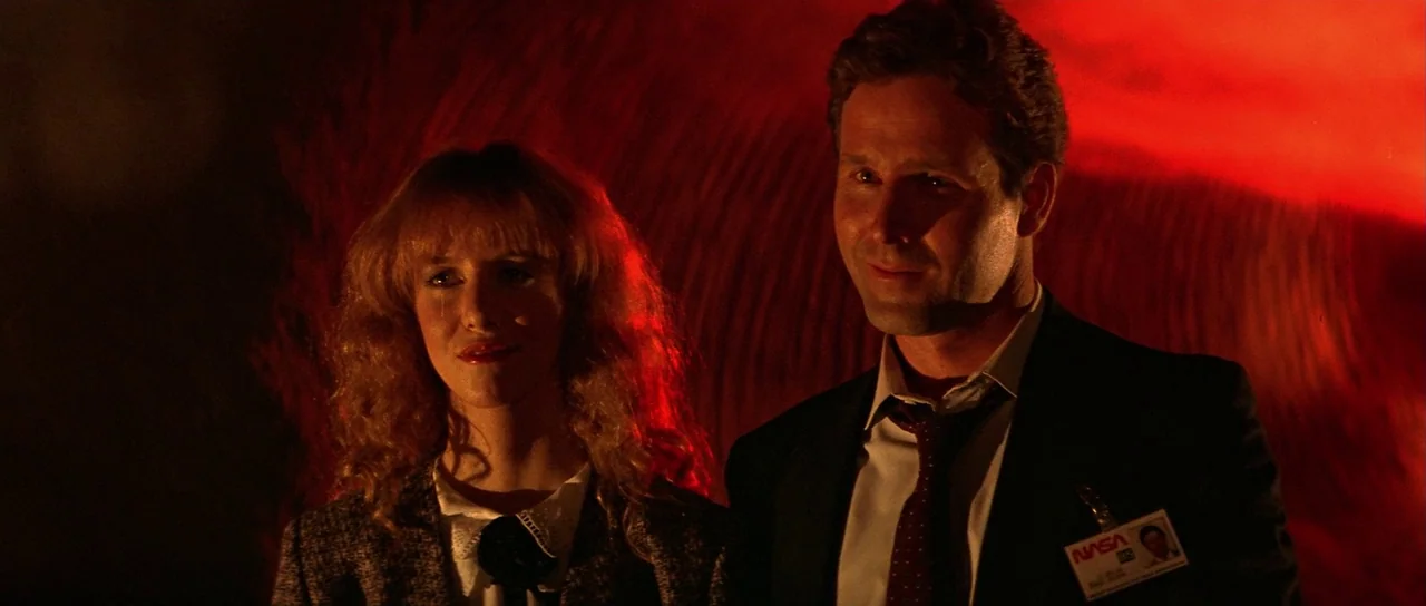 Invaders From Mars (1986) movie still: medium — A dark room is filled with intense red light against a textured wall surface. A woman and a man…
