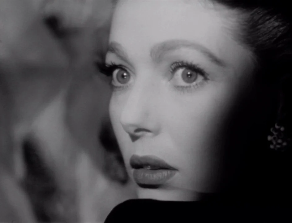 The Stranger (1946) movie still: closeup — The frame shows a tightly cropped view of a woman's face in deep shadow. She stares ahead with wide eyes…