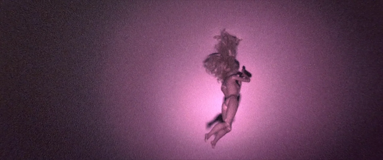 Skinamarink (2022) movie still: wide — A dark, textured void surrounds a single small plastic doll floating in center frame. The figure is…