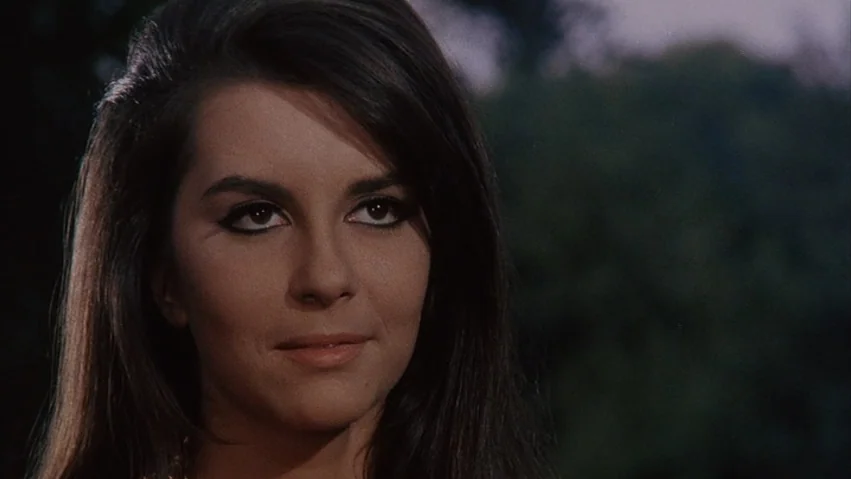 Four Times that Night (1971) movie still: closeup — An outdoor setting with a dark, out-of-focus background of trees and foliage. A young woman with…