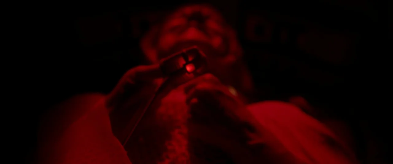 Oxygen (2021) movie still: closeup — A dark space is filled with intense red light. A person holds a small glowing device close to their chest.