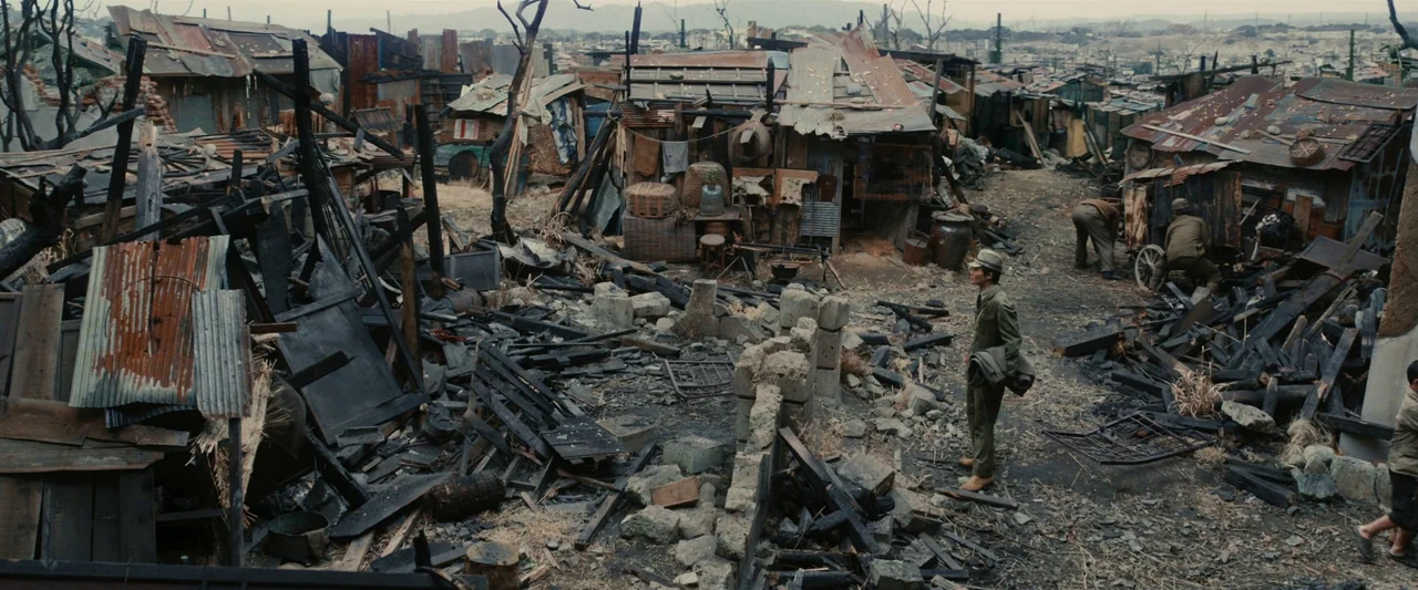 Godzilla Minus One (2023) movie still: wide — A destroyed slum filled with burnt wooden beams and rusted corrugated metal sheets. A man in a…