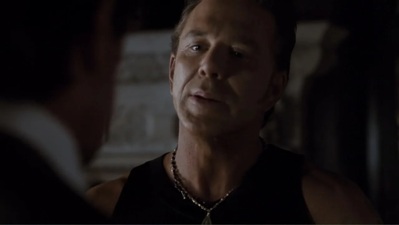 Get Carter (2000) movie still: closeup — An interior dimly lit room with blurred shadows in the background. A middle-aged man in a tank top talks to…