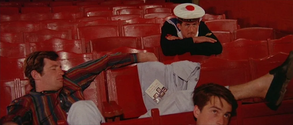 Pierrot Le Fou (Crazy Pete) (1965) movie still: medium — A rows of empty, faded red velvet seats fill a vintage cinema auditorium. Three men in…