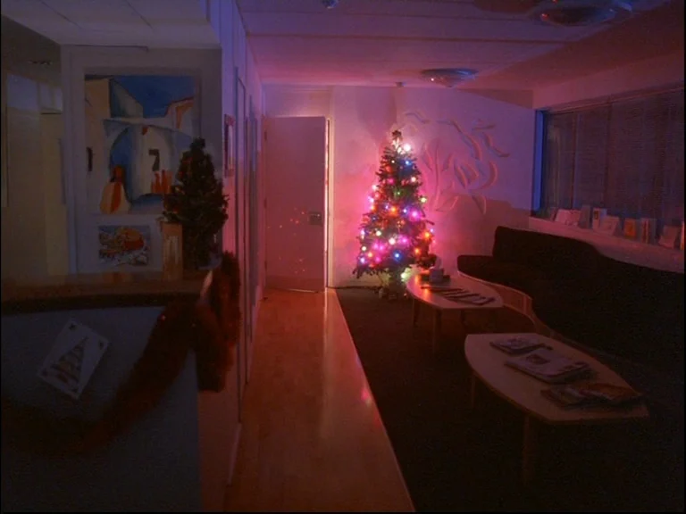 Eyes Wide Shut (1999) movie still: wide — A dimly lit waiting area features a Christmas tree with glowing colored lights. Two small coffee tables…