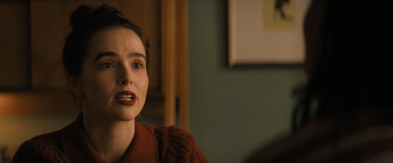 Something from Tiffany's (2022) movie still: closeup — An interior space with muted walls and a picture frame visible on the wall. A woman in a dark…