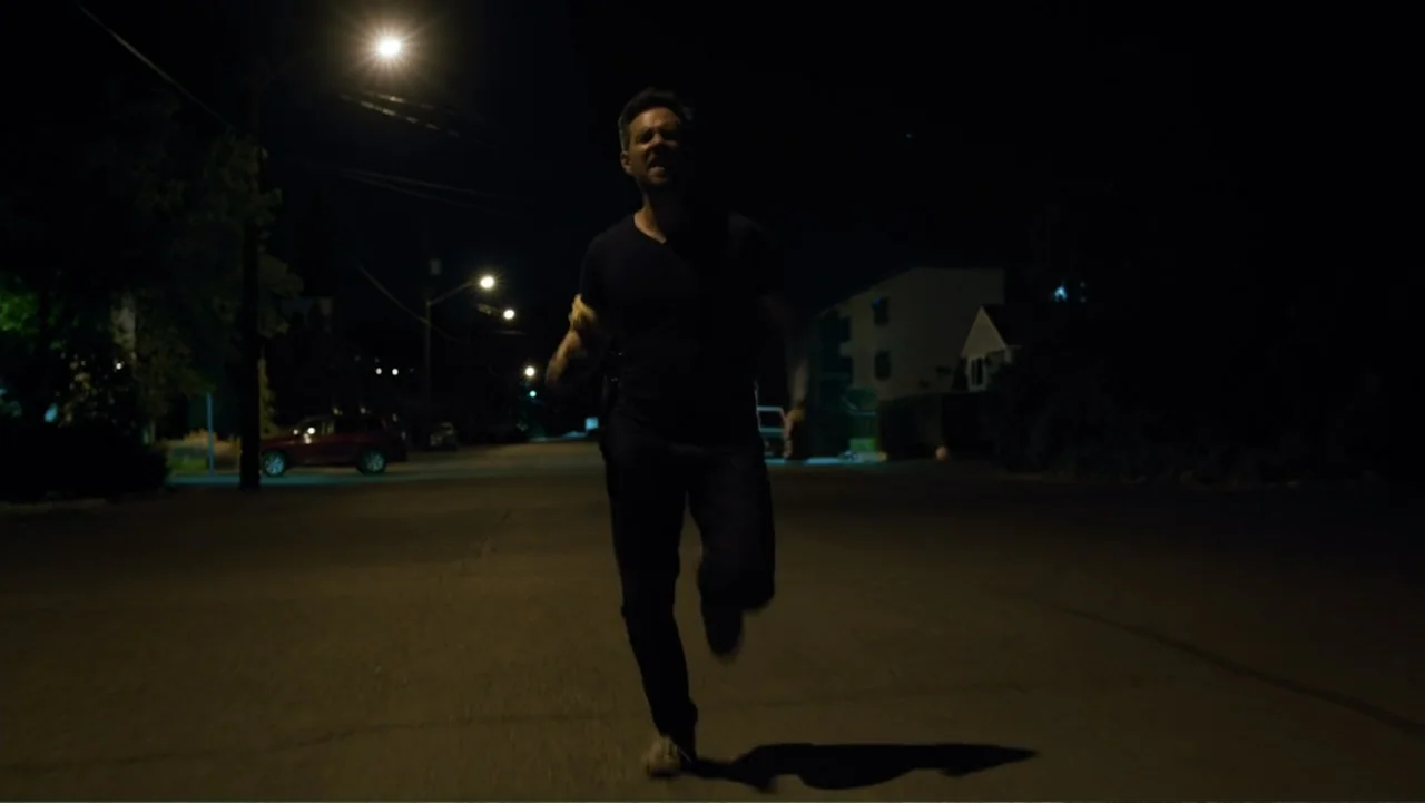Bullet Proof (2022) movie still: fullbody — A quiet residential street at night illuminated by a single distant streetlamp. A man runs towards the…