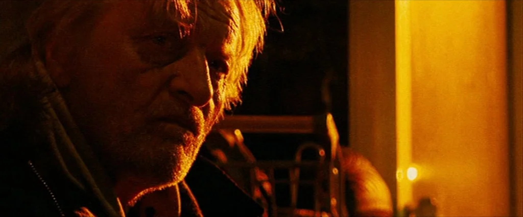 Hobo With A Shotgun (2011) movie still: closeup — An interior space is plunged into darkness with a single intense warm light source. An elderly man…