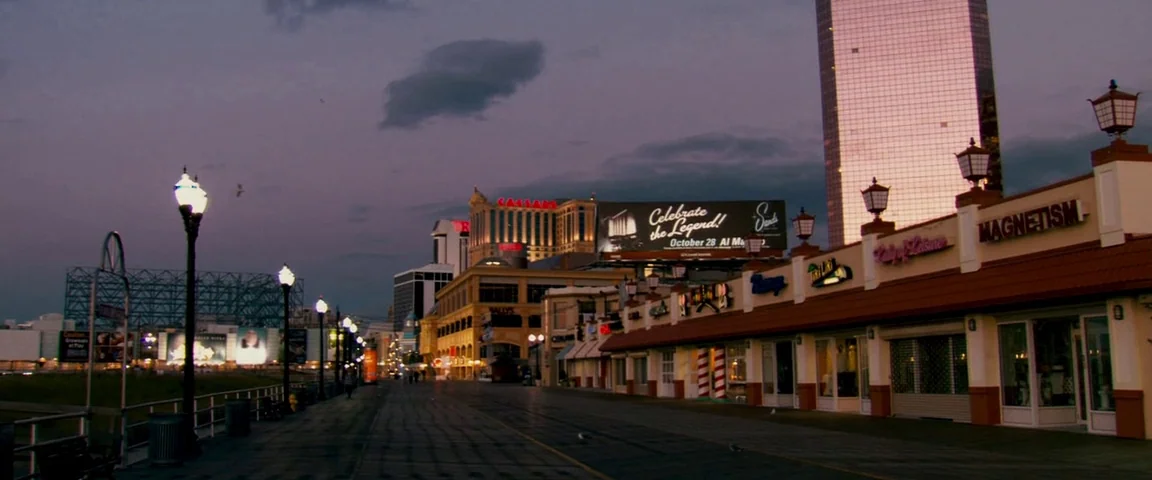The Fighter (2010) movie still: establishing — A wooden boardwalk stretches into the distance lined with closed shops and casinos. Bright city…