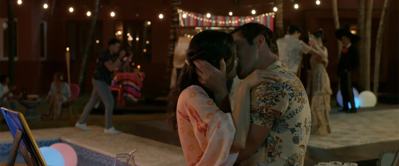 Beautiful Wedding (2024) movie still: medium — An outdoor evening gathering features a couple kissing in the foreground. Guests mingle in the…