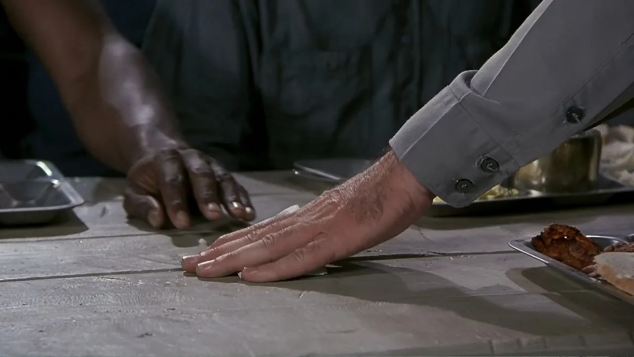 Naked Gun 33⅓: The Final Insult (1994) movie still: closeup — A wooden table in a dimly lit institutional facility holds two metal food trays. Two…