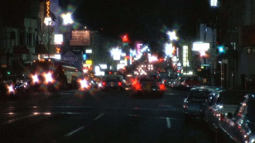 Petulia (1968) movie still: establishing — An urban boulevard at night is congested with traffic and glowing commercial signage. Numerous vehicles…