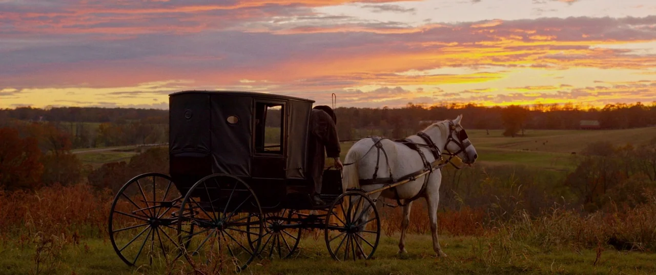 Harriet movie still: wide — A rural landscape during sunset features a horse-drawn carriage parked on a hill. A lone person in dark clothing sits in…