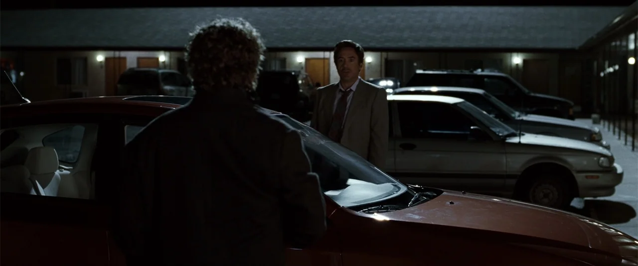 Due Date (2010) movie still: medium — A night view of a motel parking lot with cars parked in front of rooms. A man in a suit stands by a red…