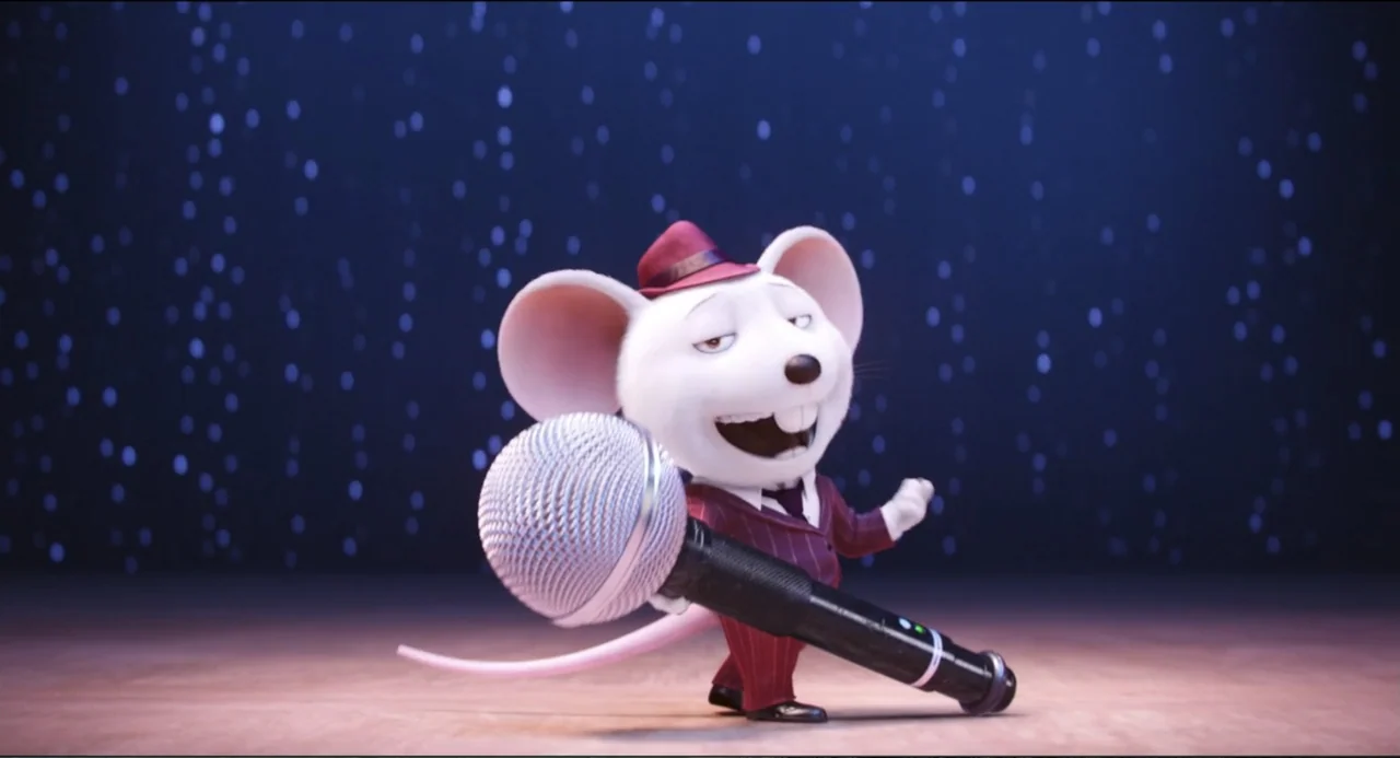 Sing (2016) movie still: medium — A cartoon white mouse stands on a wooden stage floor against a starry backdrop. The mouse holds a large microphone…