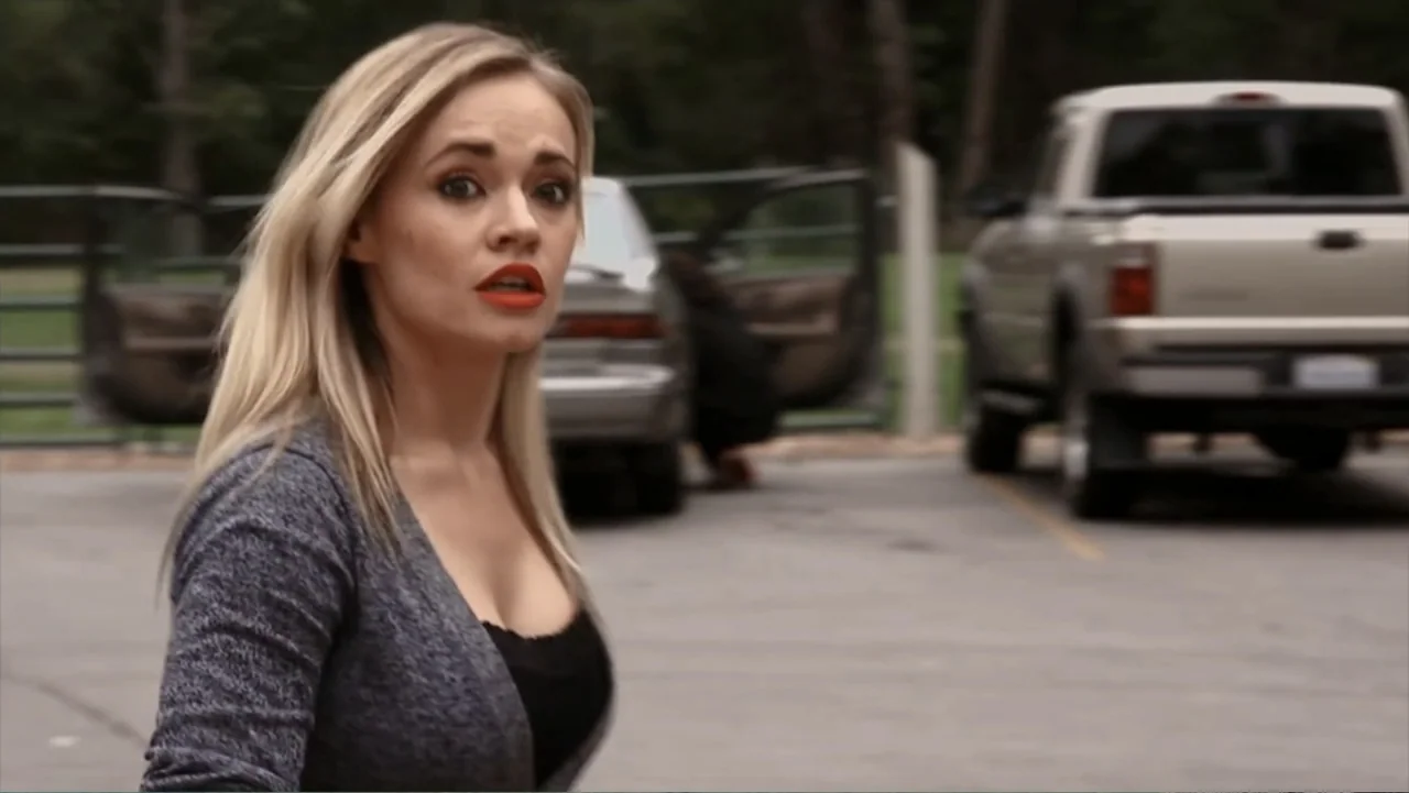 Hello I Love You (2018) movie still: medium — A paved parking lot with two vehicles parked in the background during daytime. A young woman with…