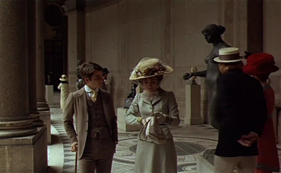 Two English Girls (1971) movie still: medium — A stone-walled interior with large columns and classical statuary on pedestals. Three people walk…