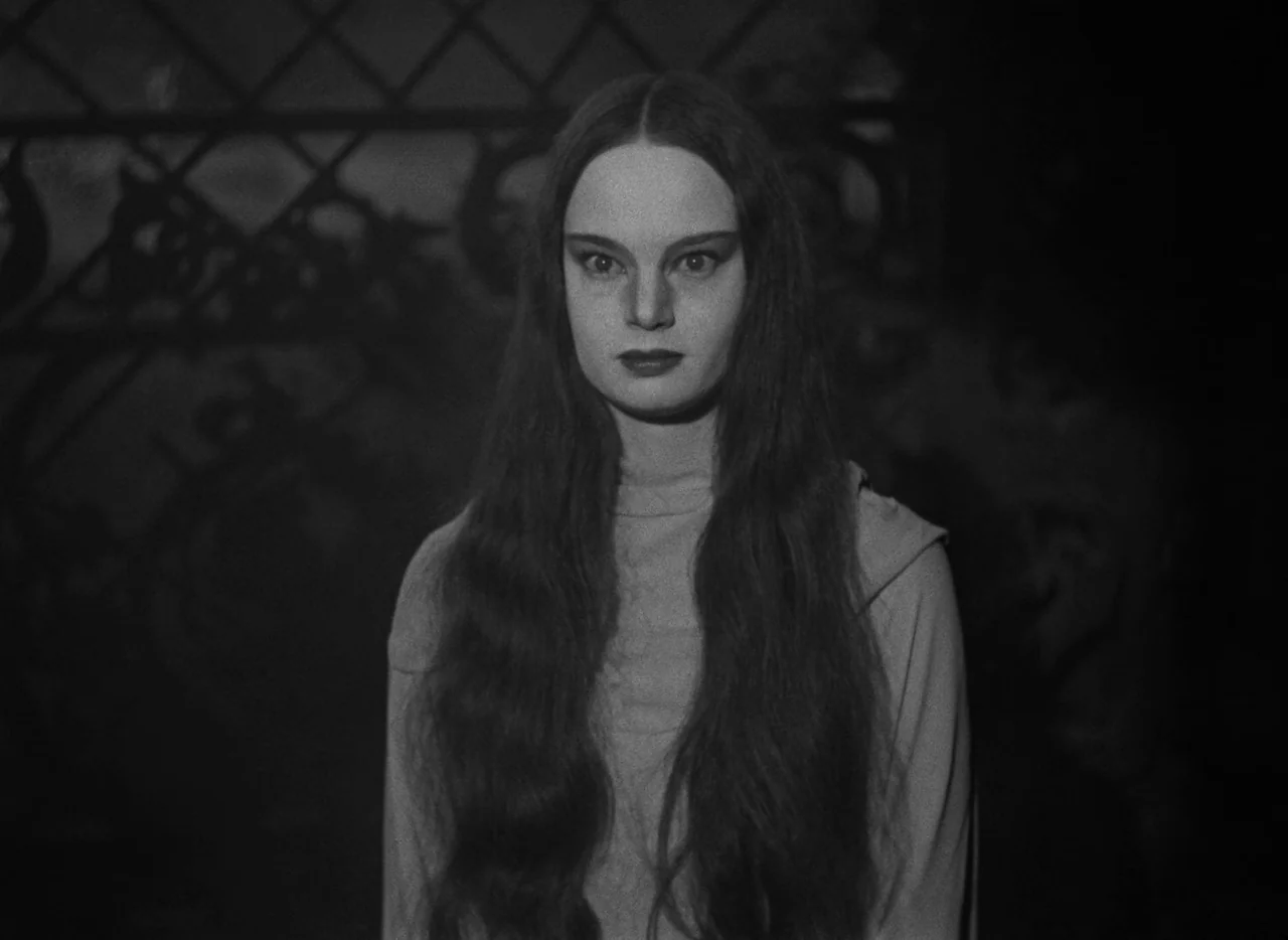 Mark of the Vampire (1935) movie still: medium — A dimly lit room with a patterned metal gate visible in the dark background. A woman with long dark…