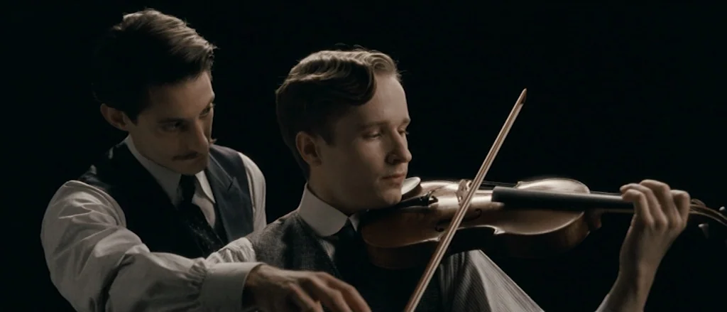 Frantz (2016) movie still: medium — A dark, nondescript room serves as the setting for two men in vintage formal attire. One man stands behind the…