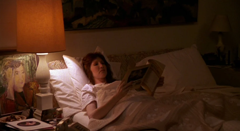 Crimes and Misdemeanors (1989) movie still: medium — A bedroom at night lit by a single bedside lamp with a tan shade. A woman with red hair rests…