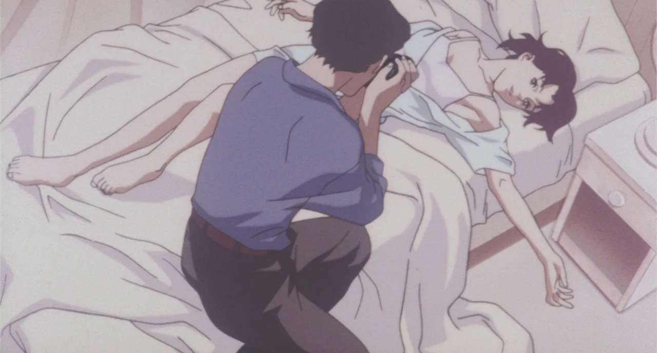 Perfect Blue (1997) movie still: medium — A bright indoor space features a bed with white sheets and a nightstand. A man in a blue shirt kneels to…