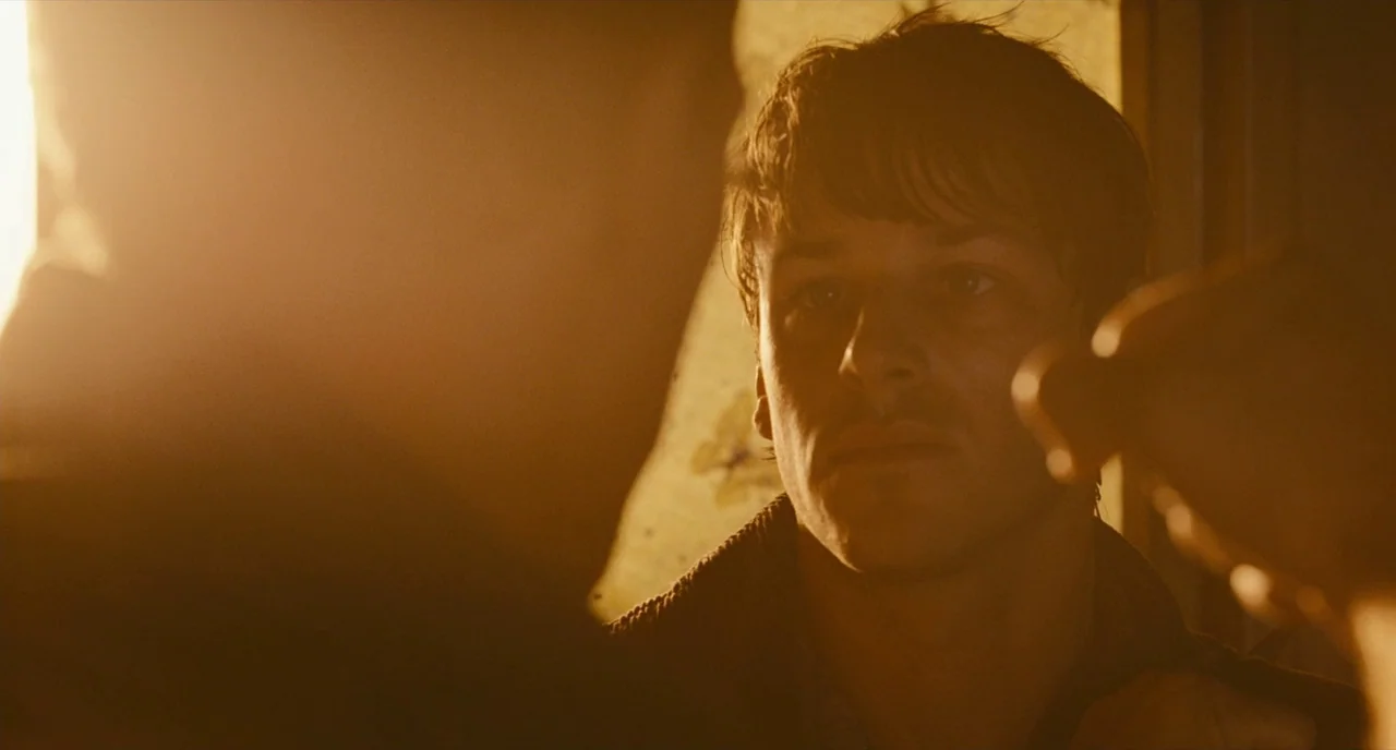 It’s Only The End Of The World (2016) movie still: closeup — A dimly lit room with textured walls bathed in golden sunlight. A young man looks…