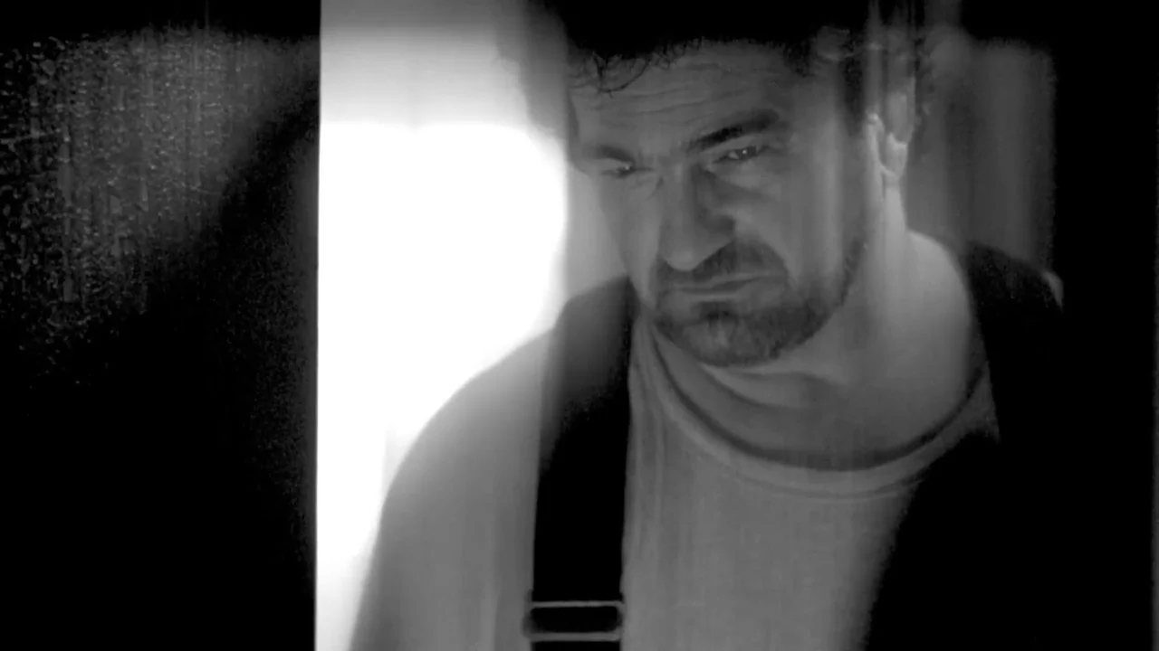 Hellraiser: Deader (2005) movie still: closeup — A man stands in a dark doorway illuminated by light from an unseen space. The subject looks down…