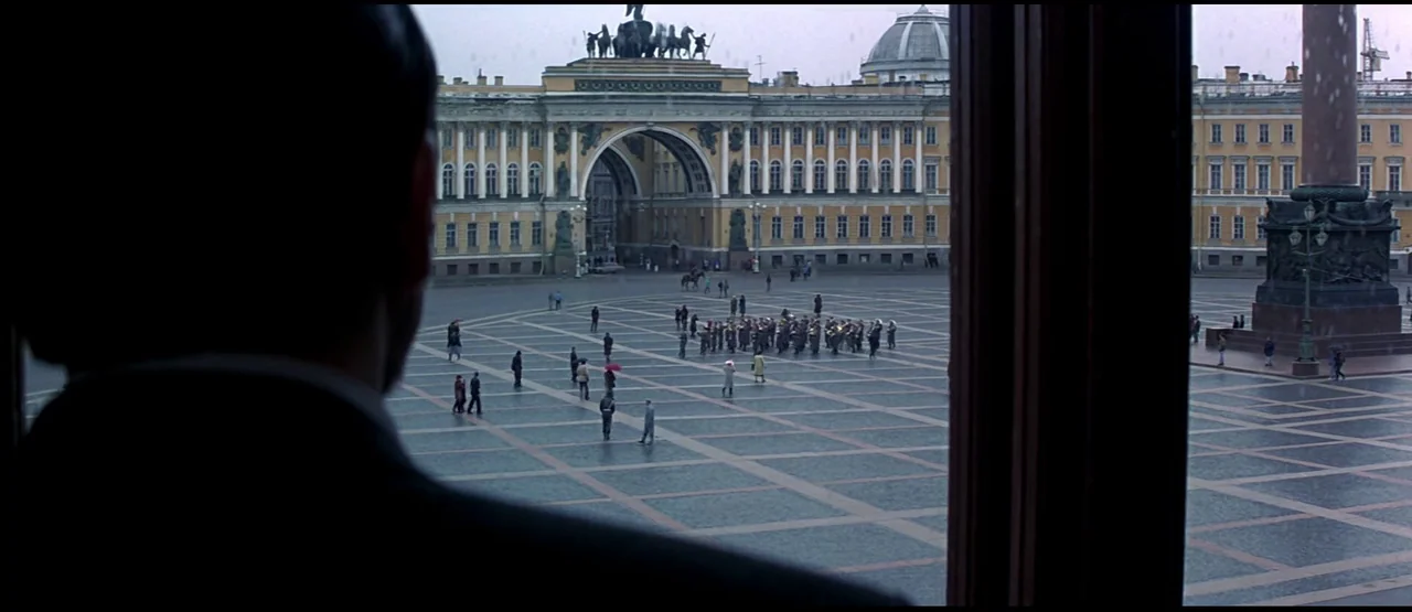 GoldenEye (1995) movie still: wide — The State Hermitage Museum and Palace Square are visible through a window frame. A small musical band performs…