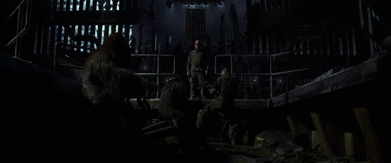 War for the Planet of the Apes (2017) movie still: wide — An abandoned industrial structure with exposed metal beams and a hanging flag. A group of…