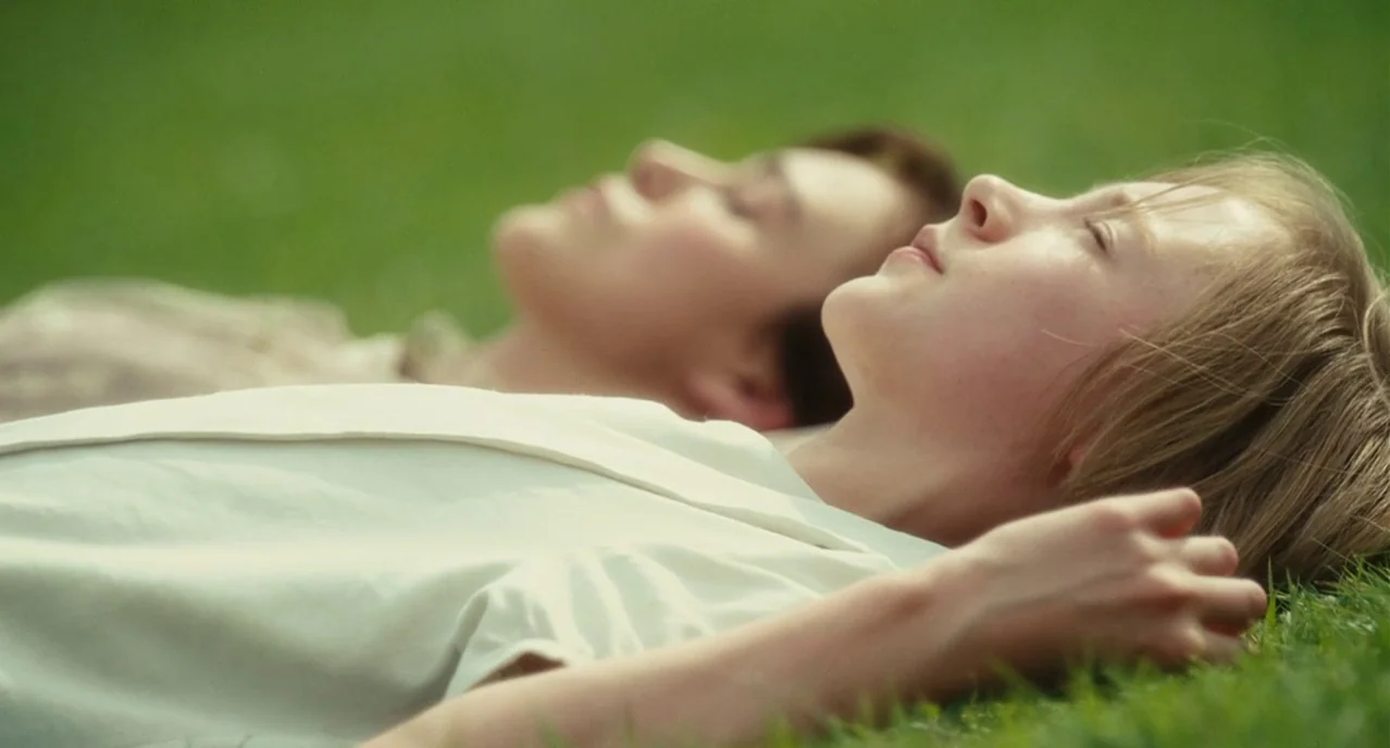 Atonement (2007) movie still: closeup — Two individuals lie side by side on a green grassy expanse. They are resting with their eyes closed in the…