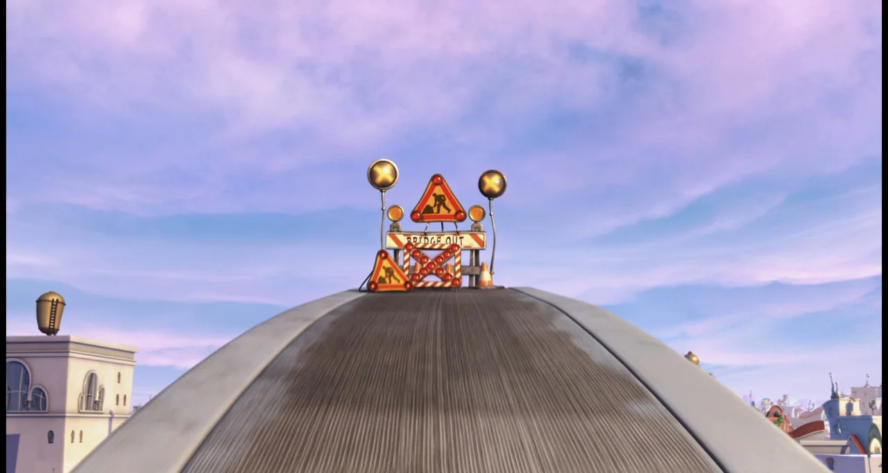 The Lorax (2012) movie still: establishing — A cartoonish paved road leads upward toward a construction barrier under a pastel sky. A stylized…