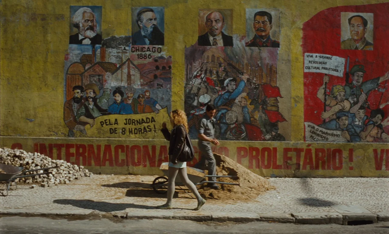 Until The End Of The World (1991) movie still: wide — A textured yellow wall features large murals of historical political figures and industrial…