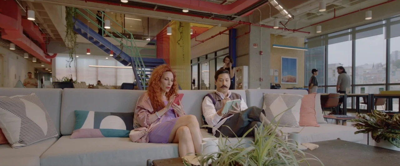 Like or Die (2023) movie still: medium — A modern open-plan office features colorful architectural accents and large floor-to-ceiling windows. A man…