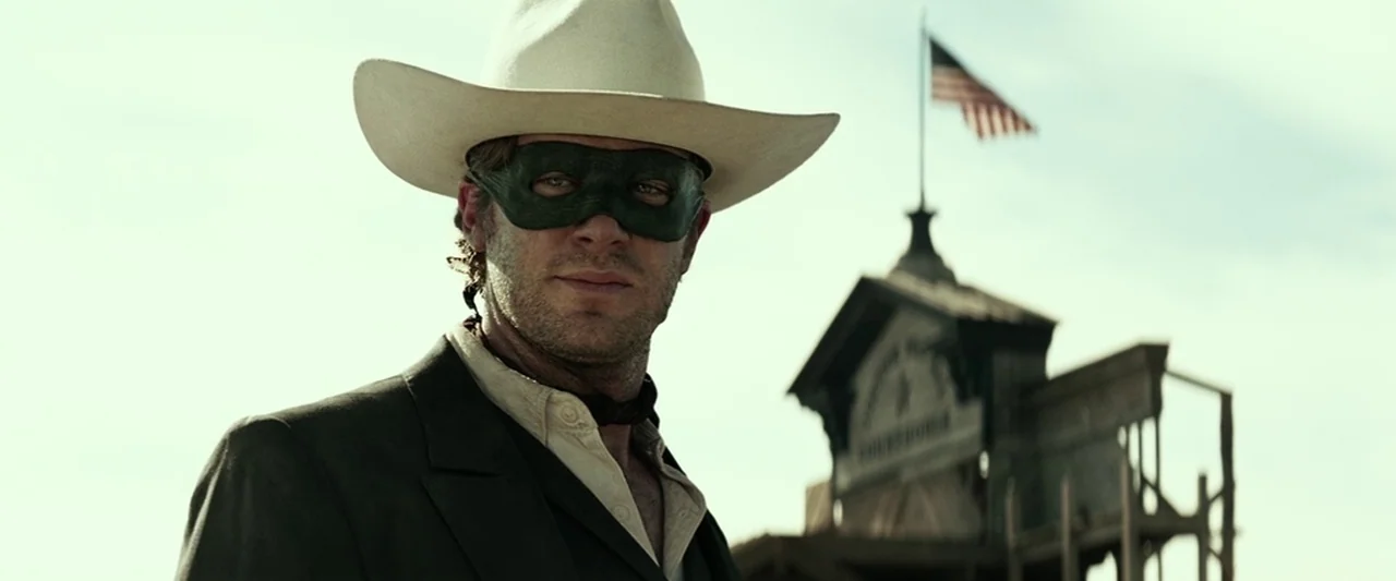 The Lone Ranger (2013) movie still: medium — A dusty outdoor town square features a classic wooden courthouse building in the background. A man in a…