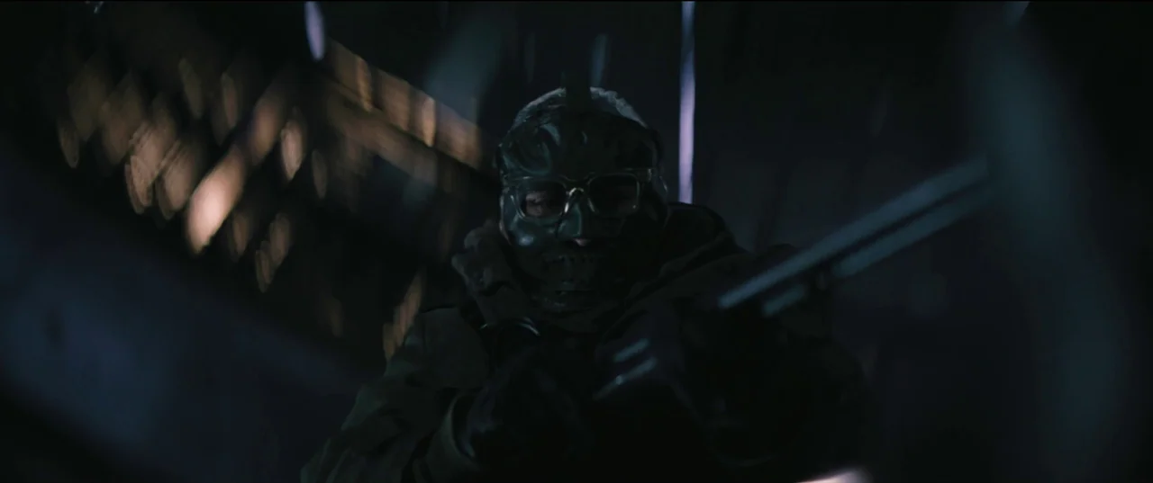 The Batman (2022) movie still: medium — A dark, wet outdoor space at night with vertical streaks of heavy rain visible. An armed individual wearing…